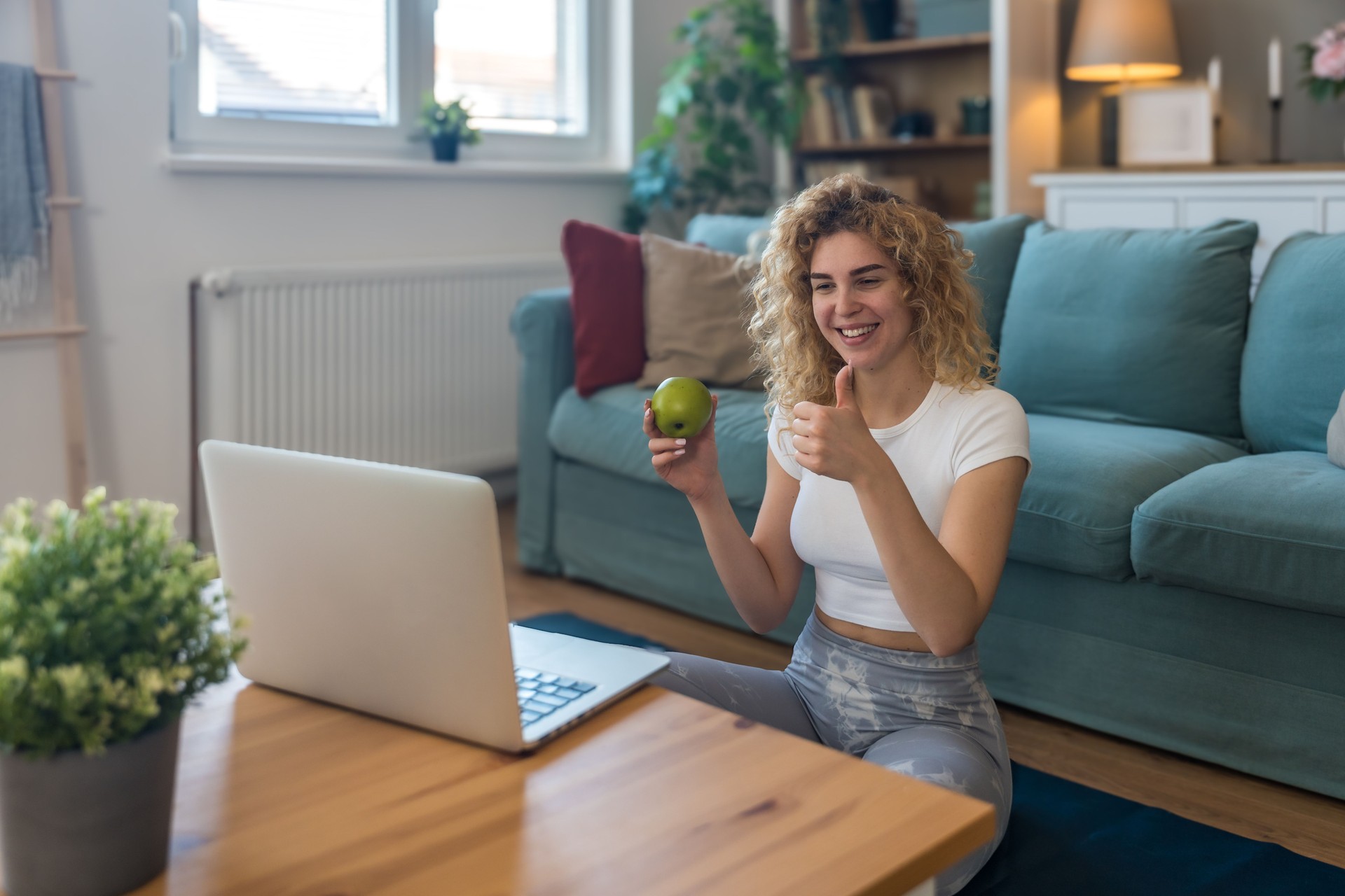 Young woman in athletic outfit doing fitness workout at home, following virtual trainer via laptop screen, focused on online exercise session, maintaining routine, motivation, and healthy lifestyle